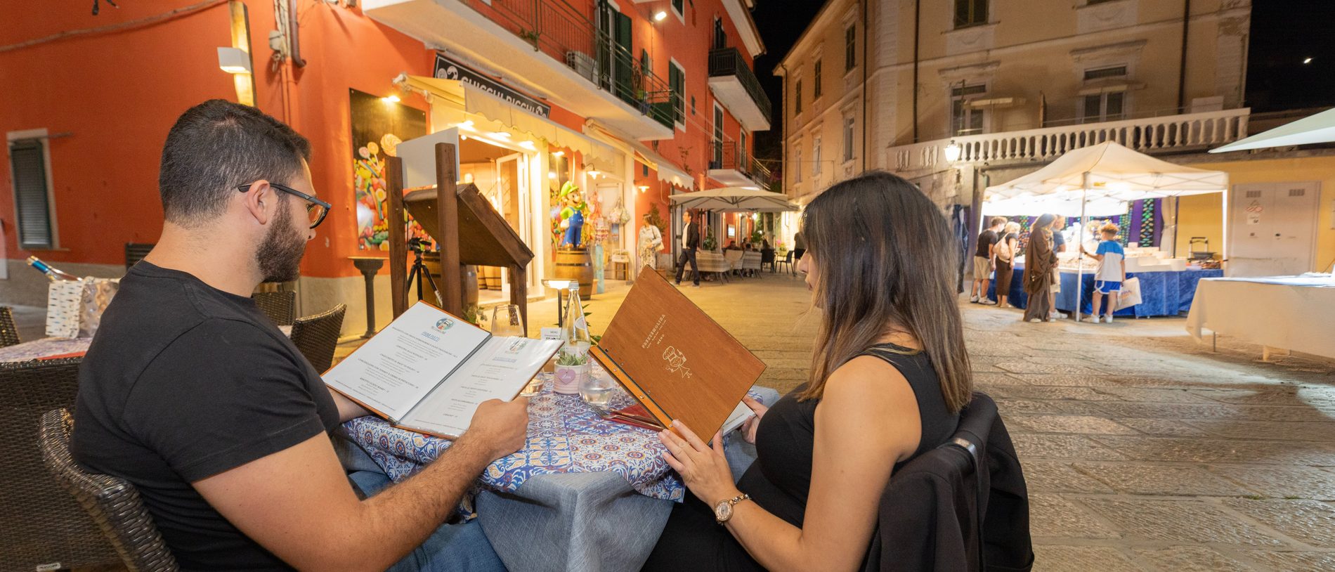 Clienti che consultano il menù ai tavoli all'aperto di sera